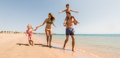 Happy parents having fun with their small kids while running on the beach. Father is carrying little boy on shoulders.